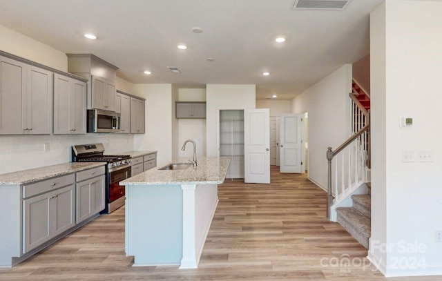 kitchen with sink, light hardwood / wood-style flooring, light stone countertops, an island with sink, and appliances with stainless steel finishes