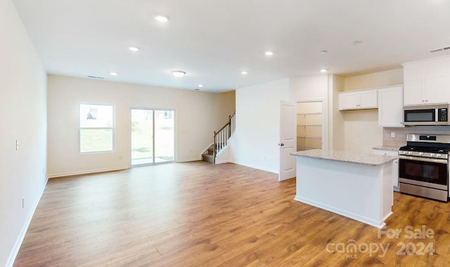 kitchen with white cabinetry, light stone counters, a center island, light wood-type flooring, and appliances with stainless steel finishes