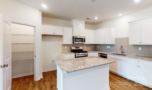 kitchen with a kitchen island, appliances with stainless steel finishes, sink, white cabinets, and light stone countertops