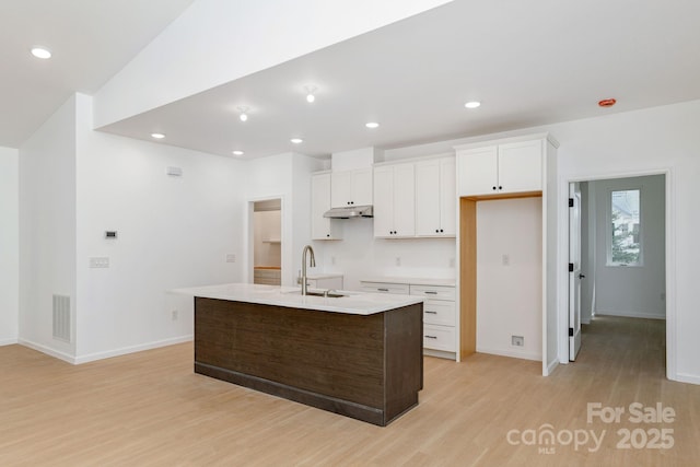 654 Hollybrook Dr, Flat Rock, NC 28731 - kitchen with light wood-type flooring, a kitchen island with sink, under cabinet range hood, white cabinetry, and recessed lighting
