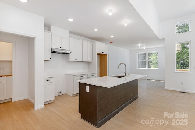 654 Hollybrook Dr, Flat Rock, NC 28731 - kitchen featuring light wood-style floors, white cabinetry, a kitchen island with sink, under cabinet range hood, and light stone counters