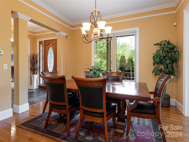 dining area featuring ornate columns, an inviting chandelier, crown molding, and hardwood / wood-style floors