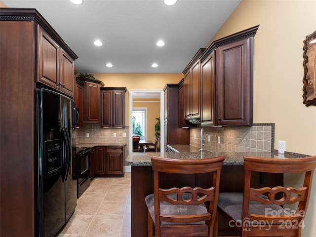 kitchen with a breakfast bar area, tasteful backsplash, light tile patterned floors, kitchen peninsula, and black appliances