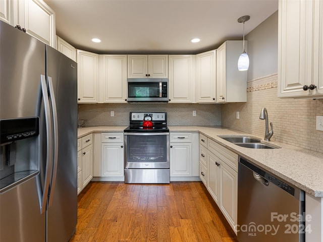 kitchen featuring stainless steel appliances, light stone countertops, decorative backsplash, wood-type flooring, and sink