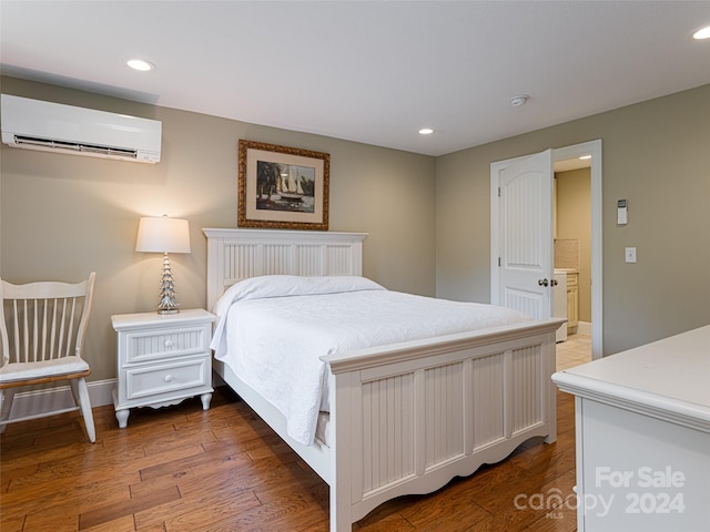 bedroom with a wall unit AC, ensuite bath, and wood-type flooring