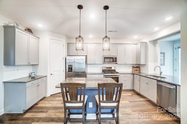 kitchen with sink, decorative light fixtures, light hardwood / wood-style flooring, dark stone counters, and stainless steel appliances