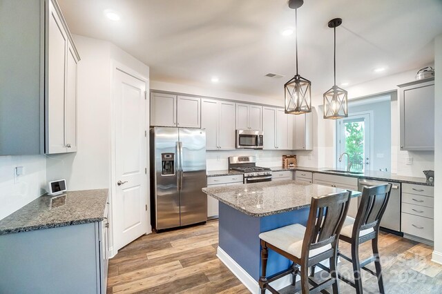 kitchen with gray cabinets, decorative light fixtures, sink, appliances with stainless steel finishes, and light hardwood / wood-style flooring