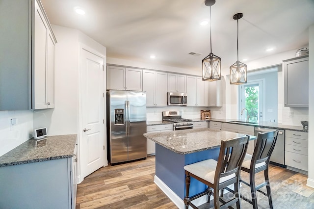 kitchen with stainless steel appliances, hanging light fixtures, sink, and light hardwood / wood-style floors