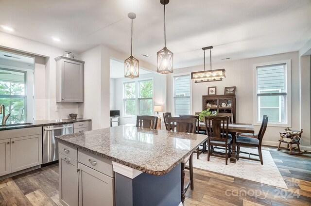 kitchen with gray cabinetry, pendant lighting, plenty of natural light, dishwasher, and hardwood / wood-style flooring