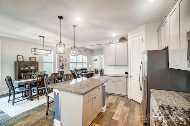 kitchen with pendant lighting, a kitchen island, hardwood / wood-style floors, and light stone counters