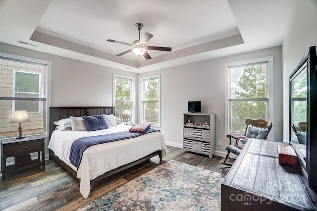 bedroom with dark wood-type flooring, multiple windows, ceiling fan, and a tray ceiling