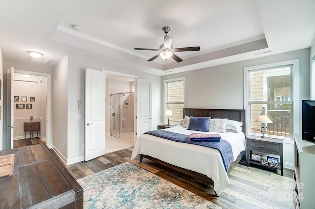 bedroom with dark wood-type flooring, ensuite bathroom, crown molding, a tray ceiling, and ceiling fan