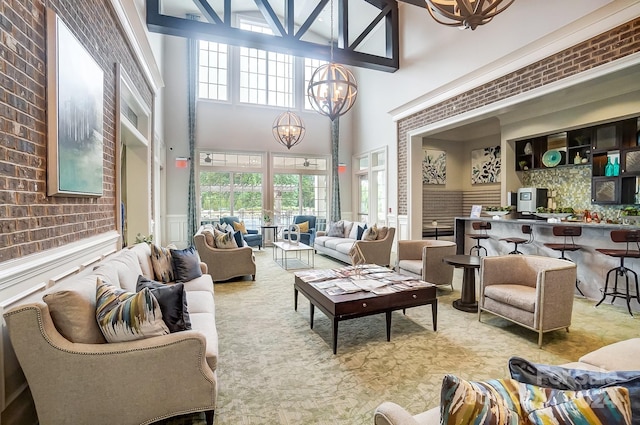 living room featuring brick wall, a towering ceiling, a wealth of natural light, and an inviting chandelier