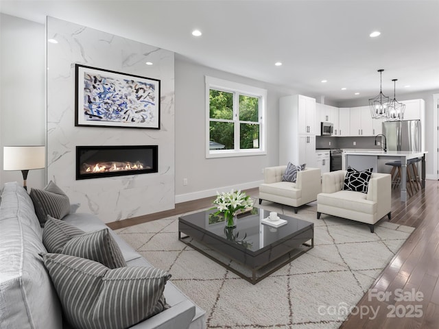 living area featuring baseboards, a premium fireplace, an inviting chandelier, light wood-style floors, and recessed lighting