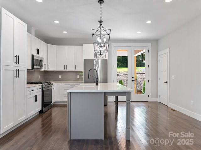 kitchen featuring appliances with stainless steel finishes, decorative light fixtures, a kitchen island with sink, light countertops, and white cabinetry