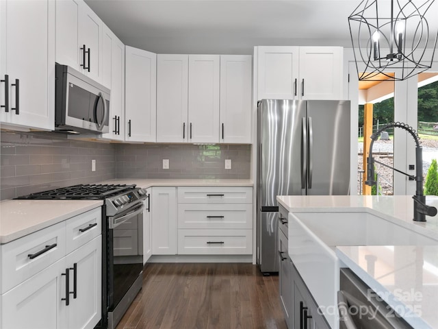 kitchen with stainless steel appliances, dark wood-type flooring, a sink, white cabinets, and pendant lighting