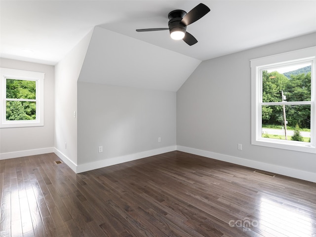 additional living space featuring dark wood-type flooring, a healthy amount of sunlight, visible vents, and vaulted ceiling