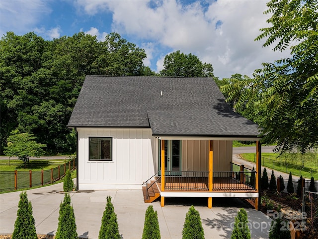 view of front of house with a patio area, fence, board and batten siding, and roof with shingles