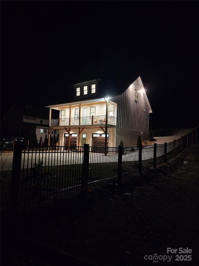 back of house at twilight featuring a balcony and a fenced front yard