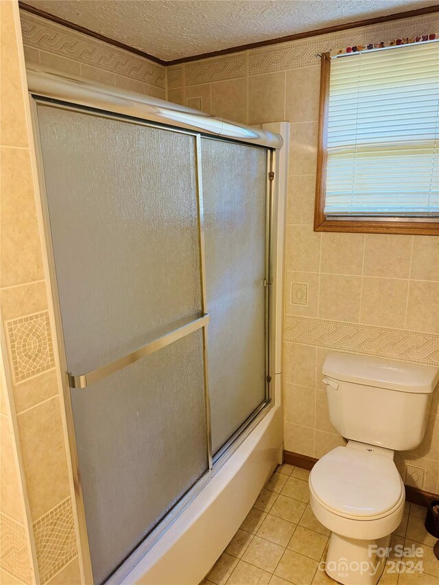 bathroom featuring toilet, combined bath / shower with glass door, tile patterned floors, and tile walls