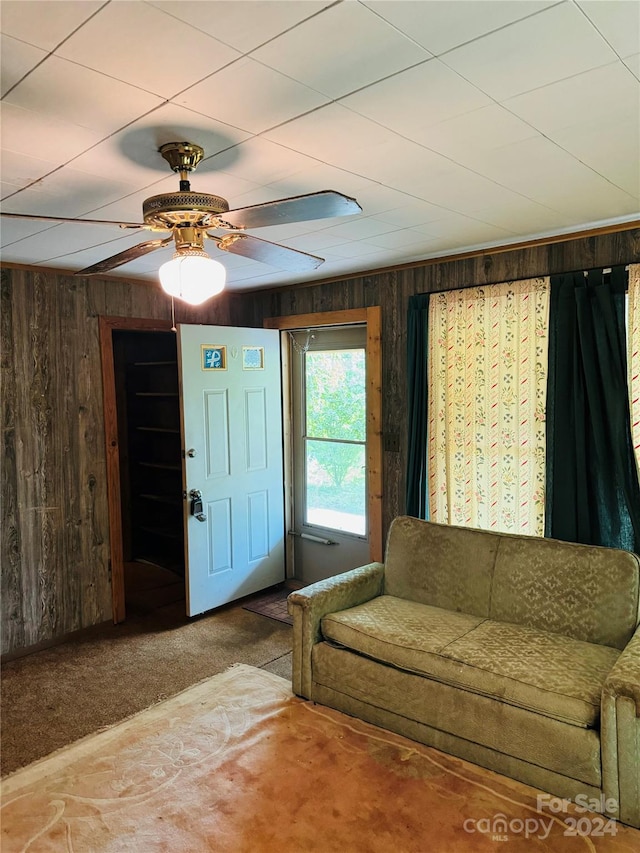 living room with ceiling fan, wood walls, and carpet floors