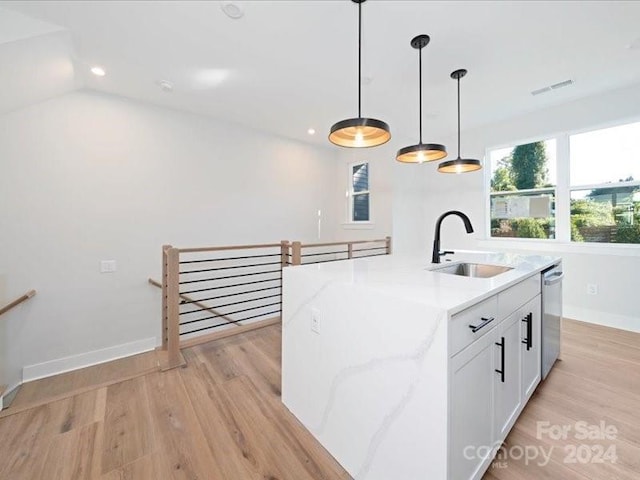 kitchen featuring a kitchen island with sink, sink, stainless steel dishwasher, light stone countertops, and white cabinetry