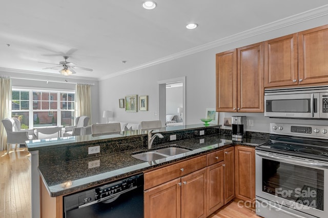 kitchen with brown cabinets, stainless steel appliances, a sink, dark stone counters, and a peninsula