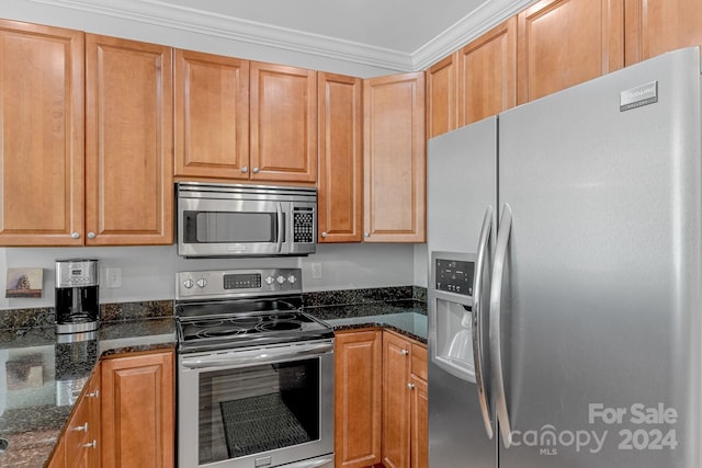 kitchen featuring stainless steel appliances, dark stone counters, brown cabinetry, and ornamental molding