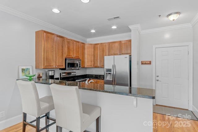 kitchen featuring visible vents, a peninsula, ornamental molding, appliances with stainless steel finishes, and light wood-type flooring