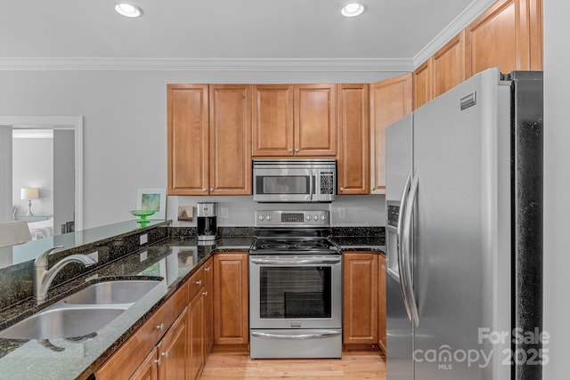 kitchen with a sink, stainless steel appliances, crown molding, and dark stone countertops