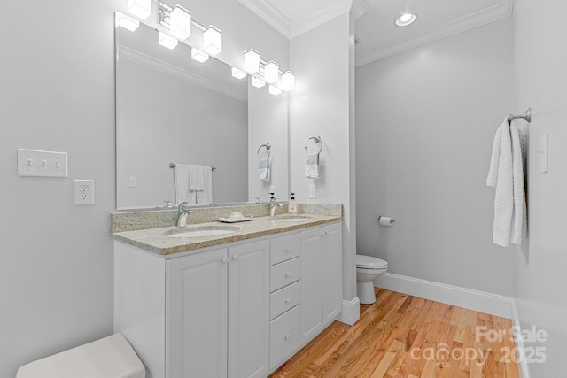 full bath with double vanity, ornamental molding, toilet, wood finished floors, and a sink