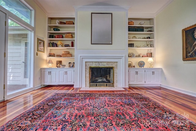 unfurnished living room with crown molding, a fireplace, built in shelves, and light hardwood / wood-style flooring