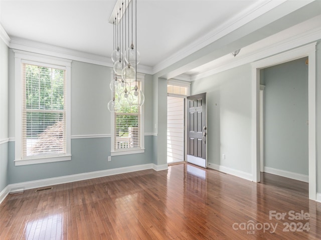 unfurnished dining area featuring a healthy amount of sunlight, ornamental molding, a notable chandelier, and hardwood / wood-style floors