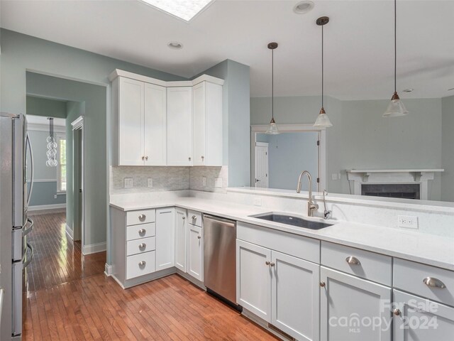 kitchen with appliances with stainless steel finishes, sink, hanging light fixtures, backsplash, and light wood-type flooring