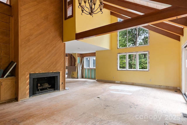 unfurnished living room featuring a notable chandelier, beamed ceiling, a fireplace, and high vaulted ceiling