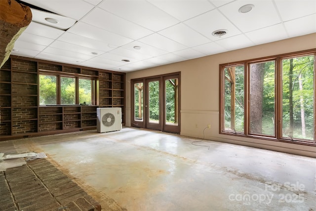 interior space with concrete floors, a drop ceiling, built in features, and a healthy amount of sunlight