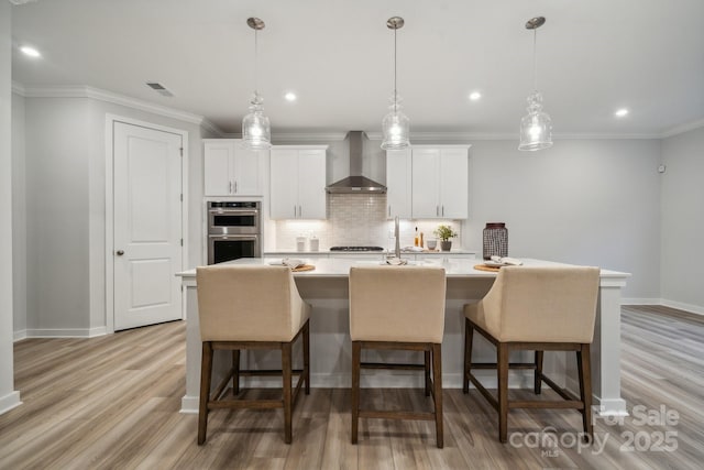 kitchen featuring white cabinets, appliances with stainless steel finishes, wall chimney range hood, tasteful backsplash, and a center island with sink