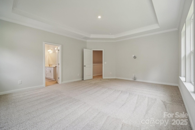 unfurnished bedroom with a tray ceiling, light carpet, ornamental molding, connected bathroom, and multiple windows