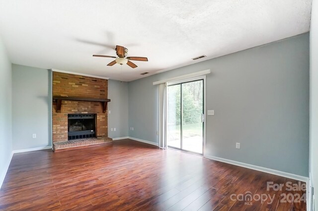 unfurnished living room with brick wall, a brick fireplace, dark hardwood / wood-style flooring, and ceiling fan