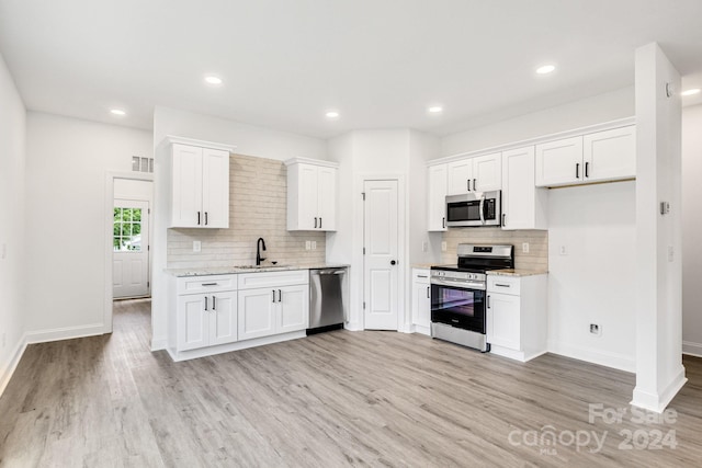 kitchen featuring stainless steel appliances, white cabinetry, light stone countertops, and sink