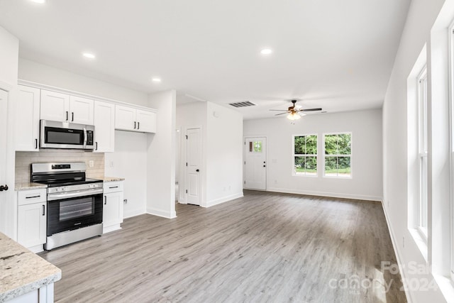 kitchen with light hardwood / wood-style flooring, appliances with stainless steel finishes, tasteful backsplash, light stone countertops, and white cabinets