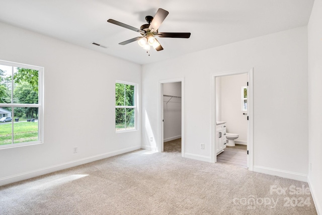 unfurnished bedroom featuring ceiling fan, connected bathroom, a walk in closet, light colored carpet, and a closet