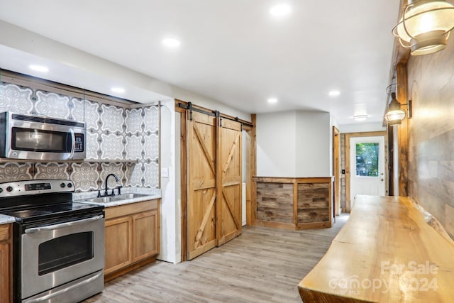 kitchen featuring butcher block counters, sink, appliances with stainless steel finishes, a barn door, and light hardwood / wood-style floors