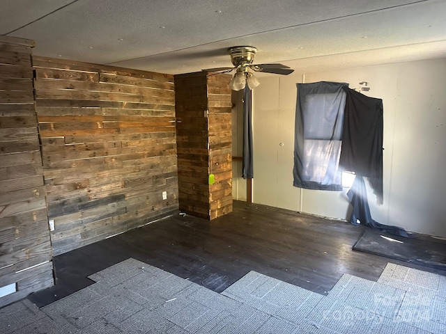 spare room featuring ceiling fan, wooden walls, and dark hardwood / wood-style floors