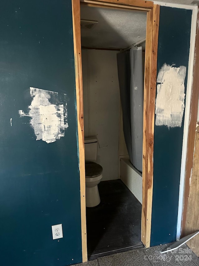 bathroom featuring toilet, a textured ceiling, and shower / bath combo with shower curtain