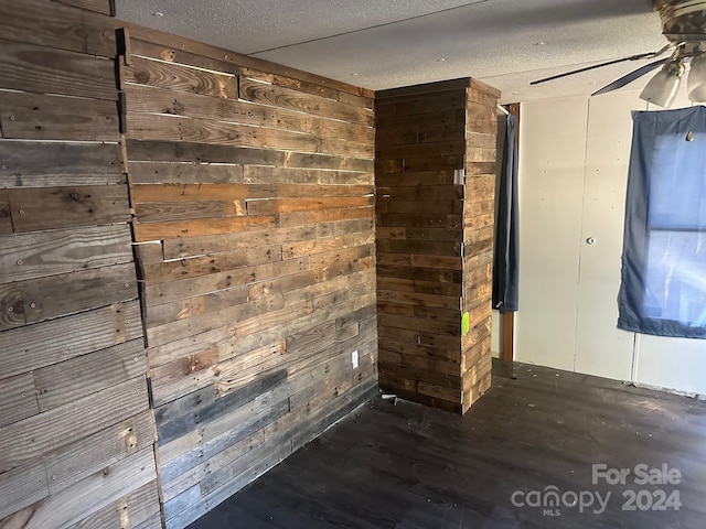 unfurnished room featuring wood walls, ceiling fan, a textured ceiling, and dark hardwood / wood-style floors