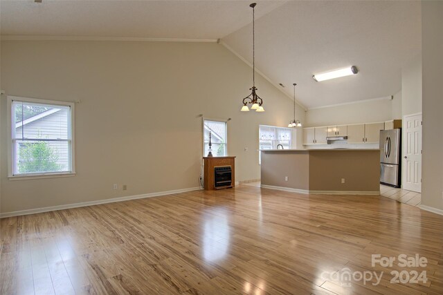 unfurnished living room featuring a notable chandelier, light wood-type flooring, and high vaulted ceiling