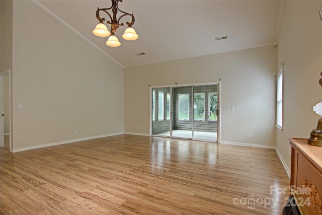 unfurnished living room with light hardwood / wood-style flooring, a notable chandelier, crown molding, and vaulted ceiling