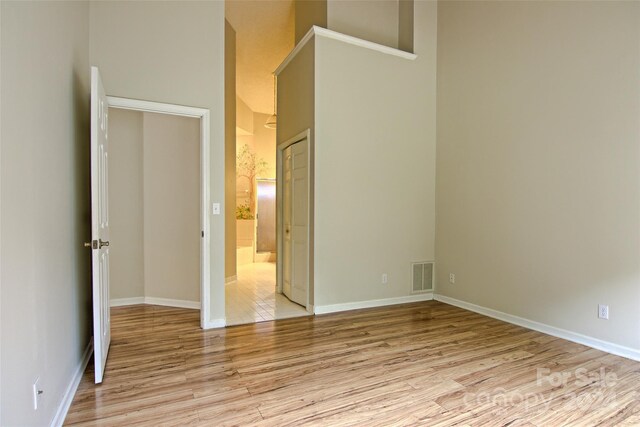 unfurnished bedroom with a towering ceiling, ensuite bath, and light hardwood / wood-style floors