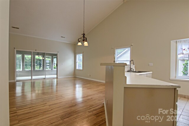 kitchen with light hardwood / wood-style flooring, ornamental molding, hanging light fixtures, and high vaulted ceiling